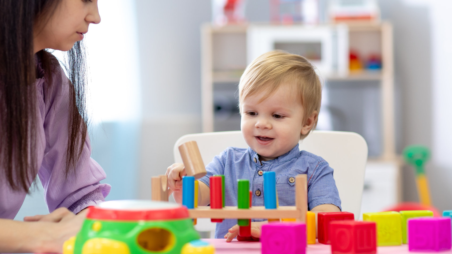 Nursery baby and caregiver play with montessori toys at table in daycare centre